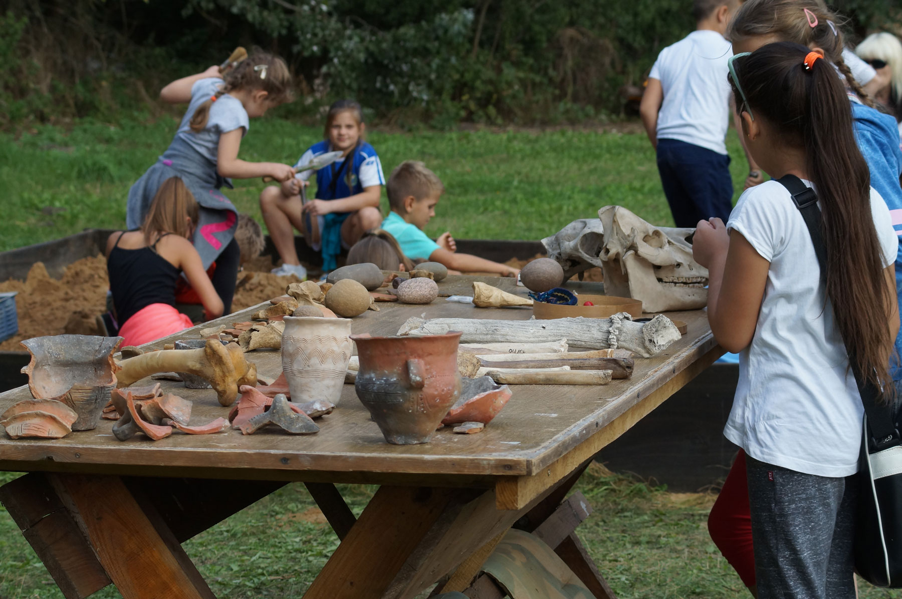 Dzieci bawiące się w małego archeologa, na stole kawałki glinianych naczyń, kość zwierzęca 