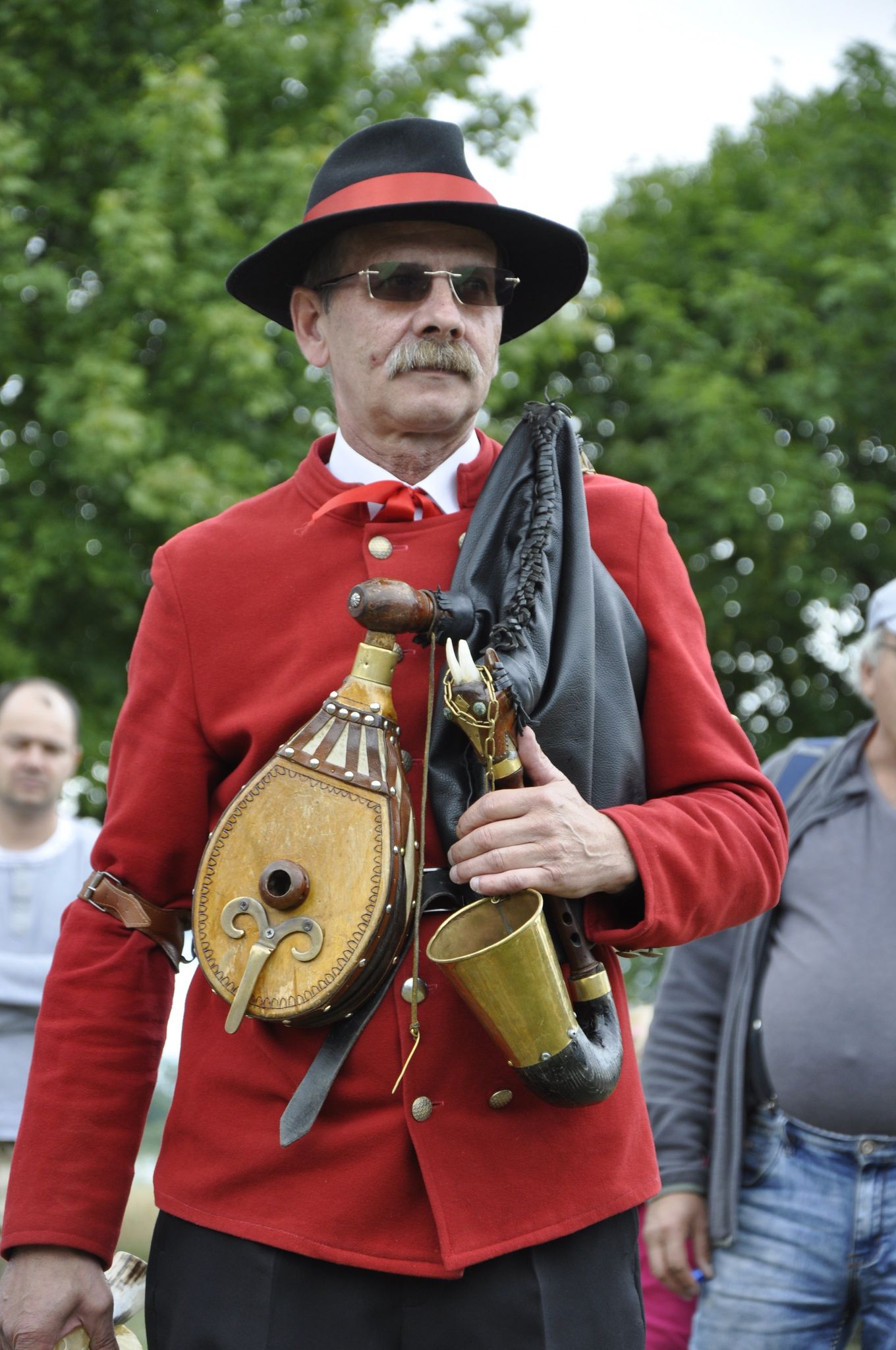 Mężczyzna w czarnym kapeluszu z czerwoną wstążką, ciemnych okularach i czerwonej marynarce 