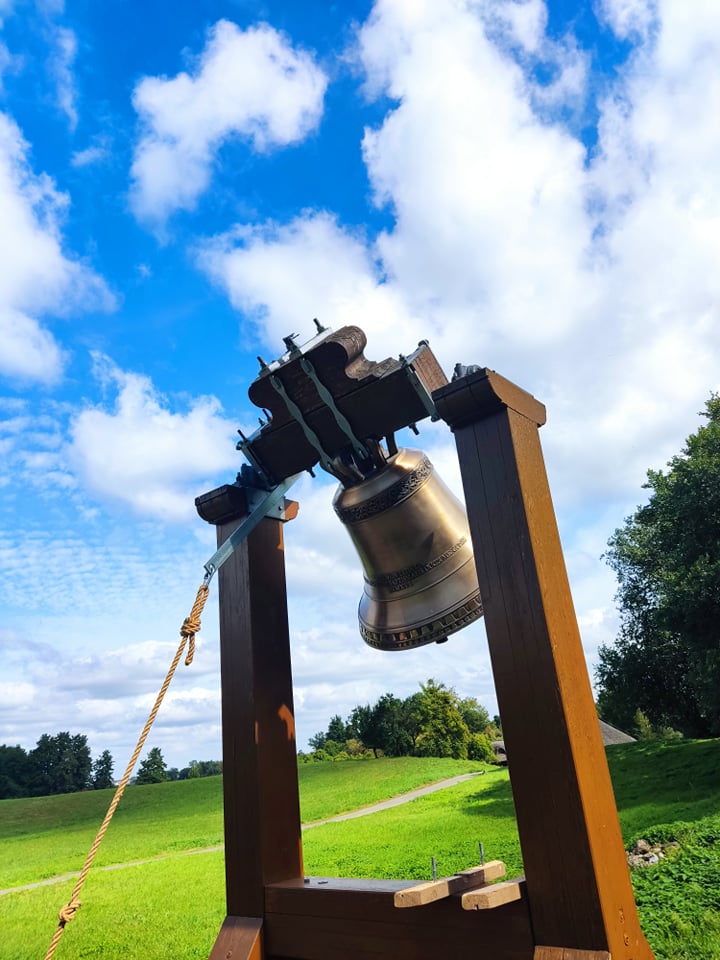 Dzwon umieszczony na drewnianej konstrukcji w tle niebieskie niebo i białe chmury