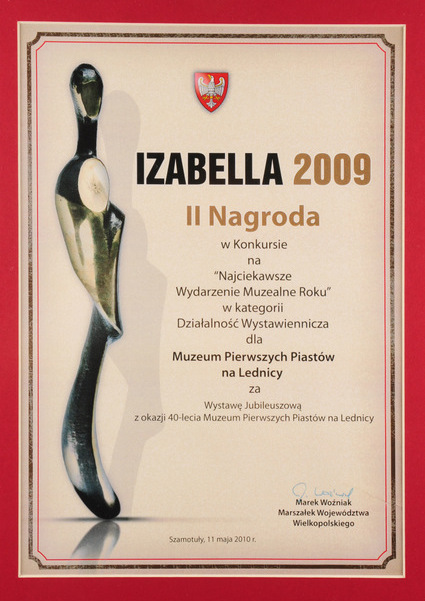 Dyplom z czerwoną otoczką nagrody Izabella z widoczną statuteką  po lewej stronie