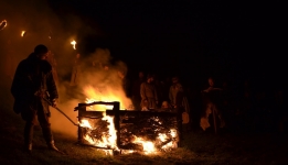 Grupa ludzi stojących z pochodniami, mężczyzna podpalający ognisko 