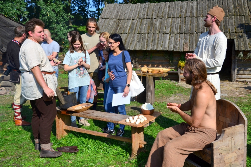 W grodzie w Grzybowie rekonstruktorzy historyczni podczas przyrządzania średniowiecznej strawy, w tle grupa turystów.