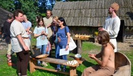 W grodzie w Grzybowie rekonstruktorzy historyczni podczas przyrządzania średniowiecznej strawy, w tle grupa turystów.
