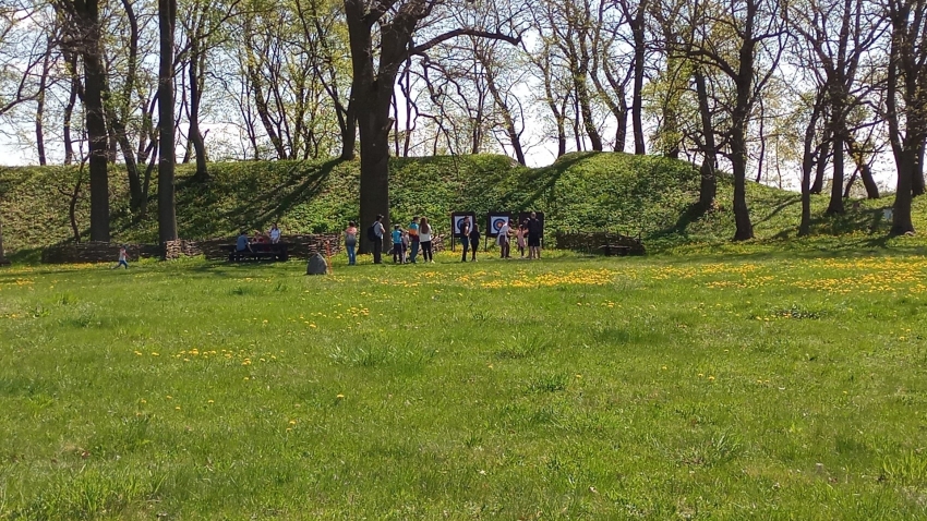 Zielona trawa, grupka uczestników przy tarczy do  strzelania z łuku. 